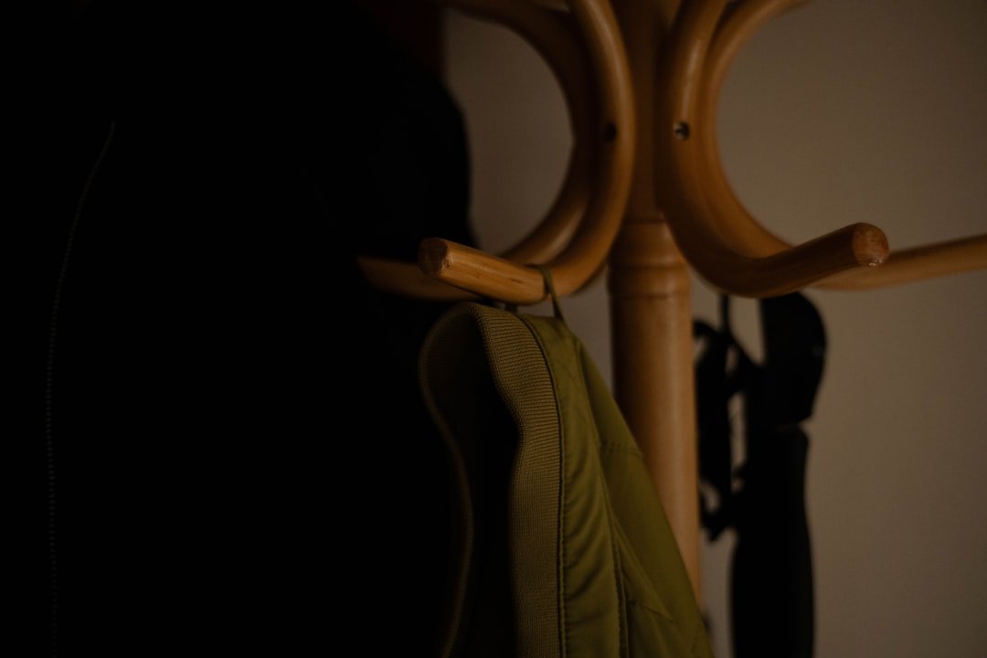 Wooden entryway coat rack with hooks holding a jacket, part of a bench and hook storage setup