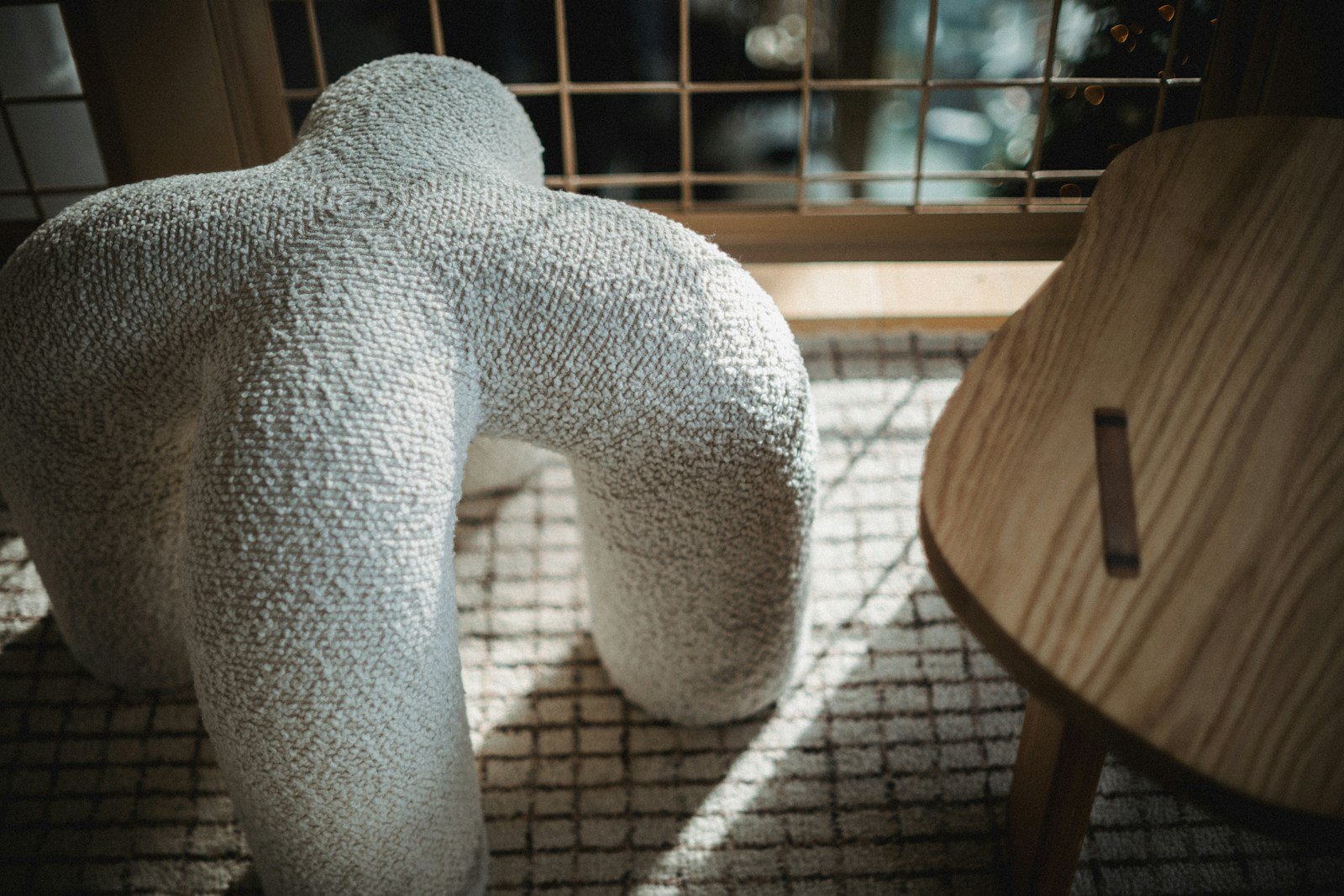 Layered texture in a neutral living room with a wooden chair and sculptural decor beside a window