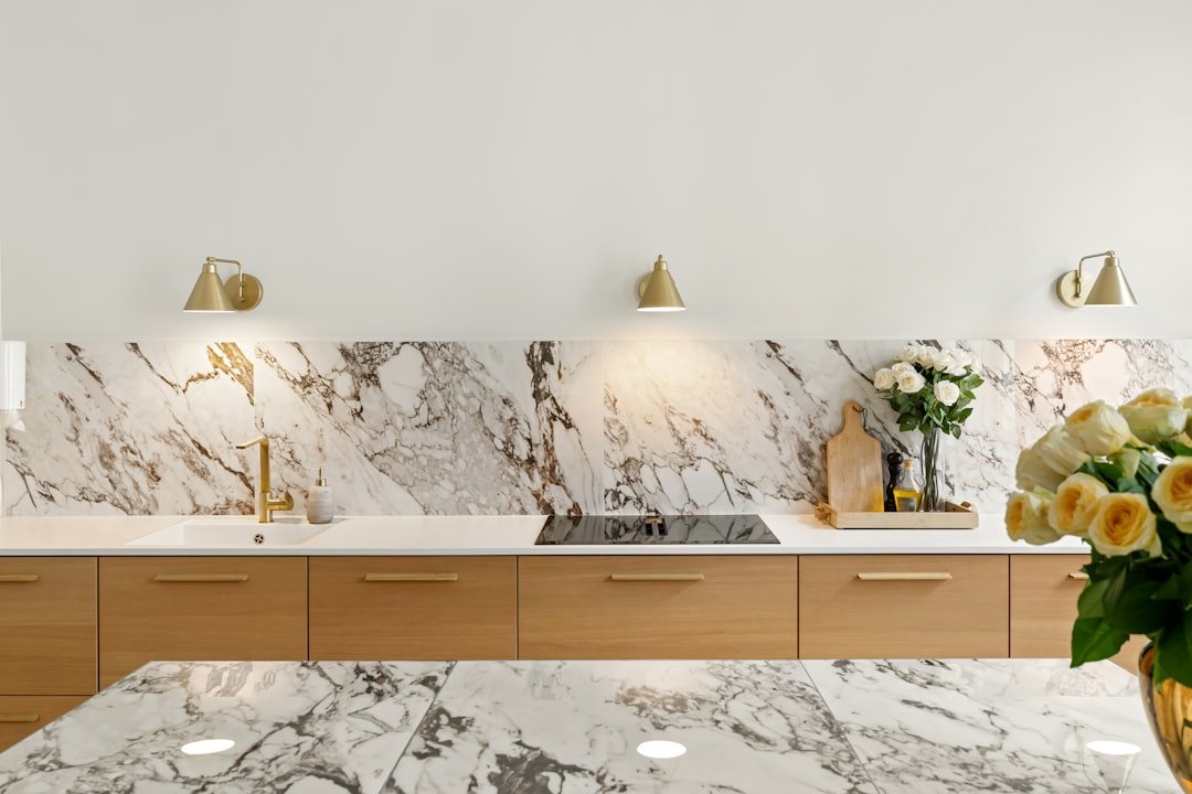 Marble countertops and backsplash with gold accents in a white kitchen, adding texture without color
