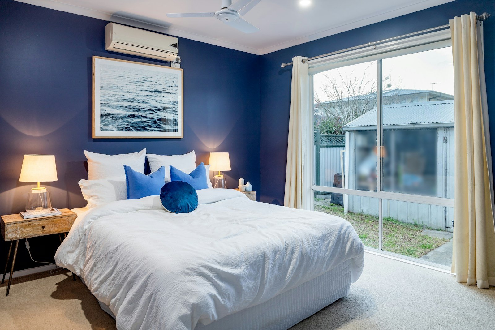 Deep navy blue bedroom walls with a white bed, an example of dark bedroom colors