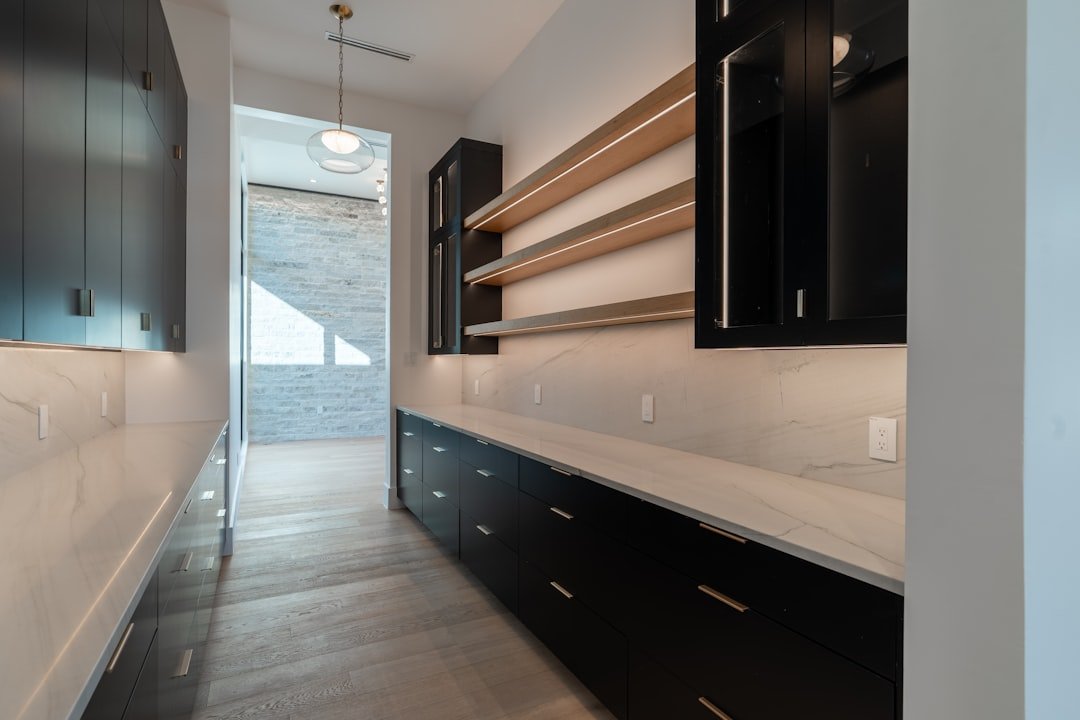 Pantry organization with dark painted cabinets, light counters and warm wood shelves