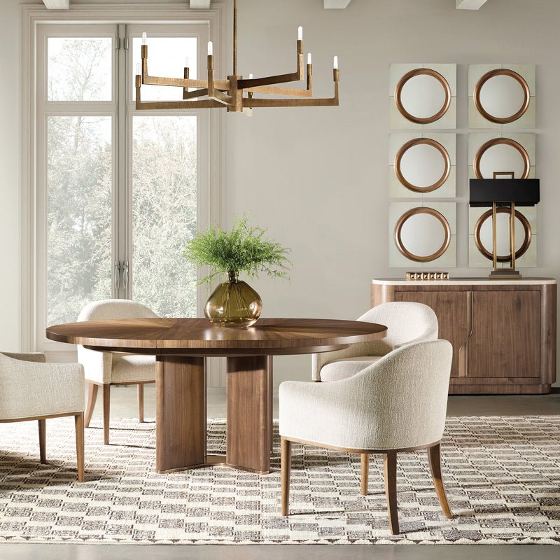 Round walnut dining table with curved upholstered chairs, neutral rug, and modern chandelier