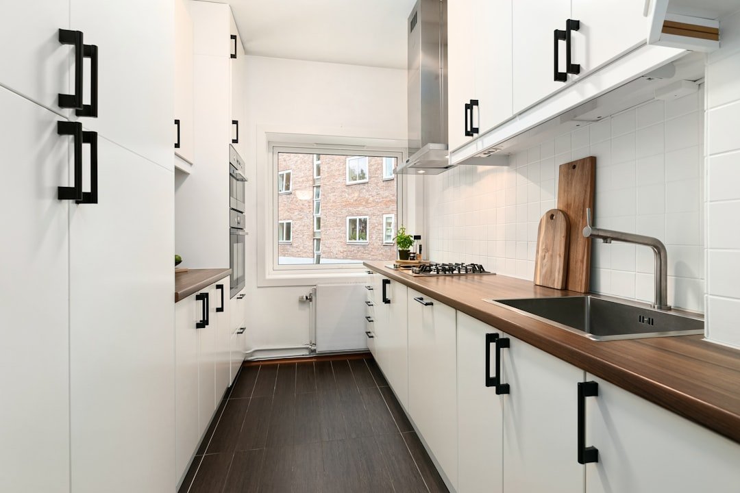Narrow small white kitchen with white cabinets and wood countertops in an apartment
