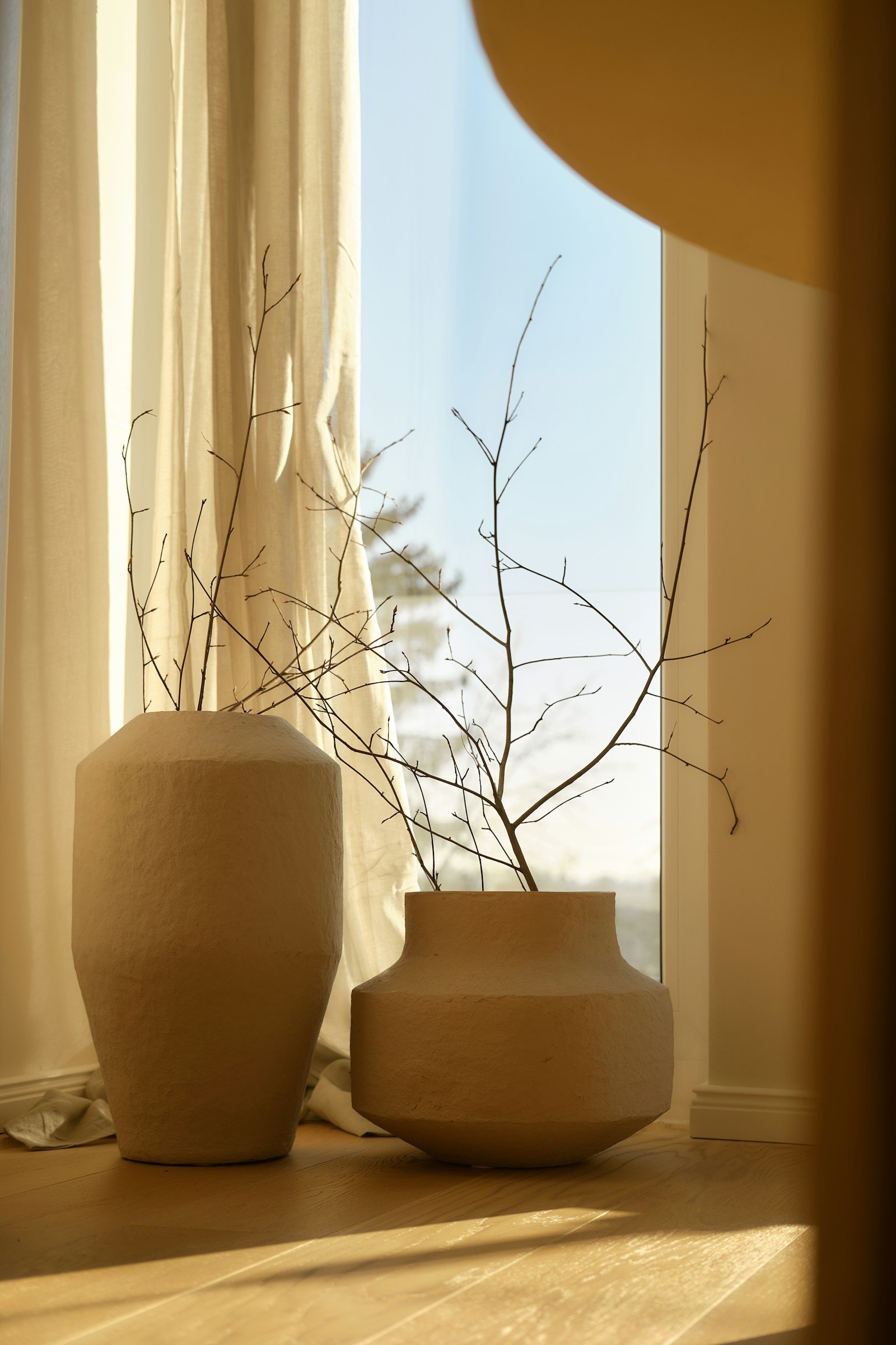 Beige decor accents, two textured ceramic vases with dried branches grouped by a window