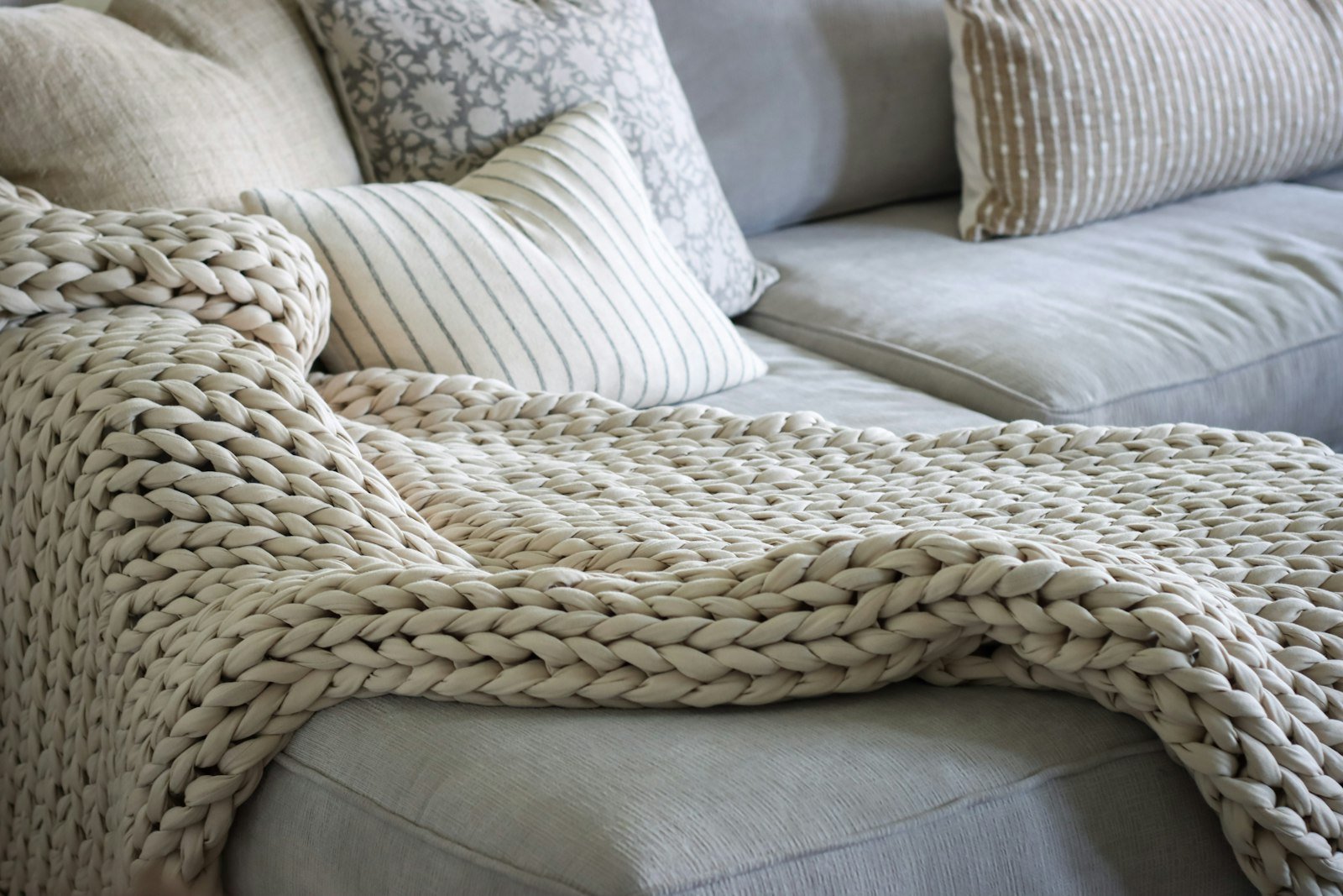 Chunky knit throw blanket layered over a sofa to add texture in an apartment