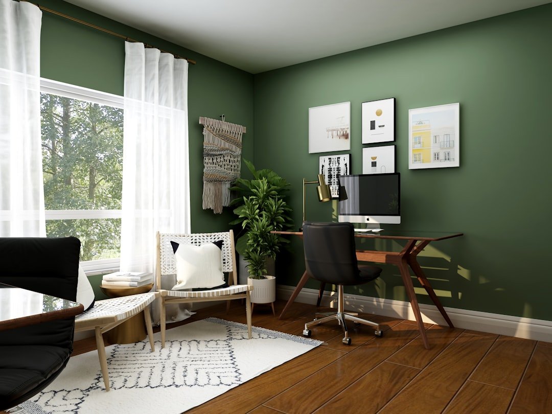 Home office with a wood desk, black chair, green walls, and warm natural decor