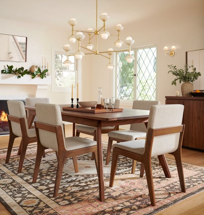 Warm dining room with a walnut table, upholstered chairs, patterned rug, and sculptural brass chandelier