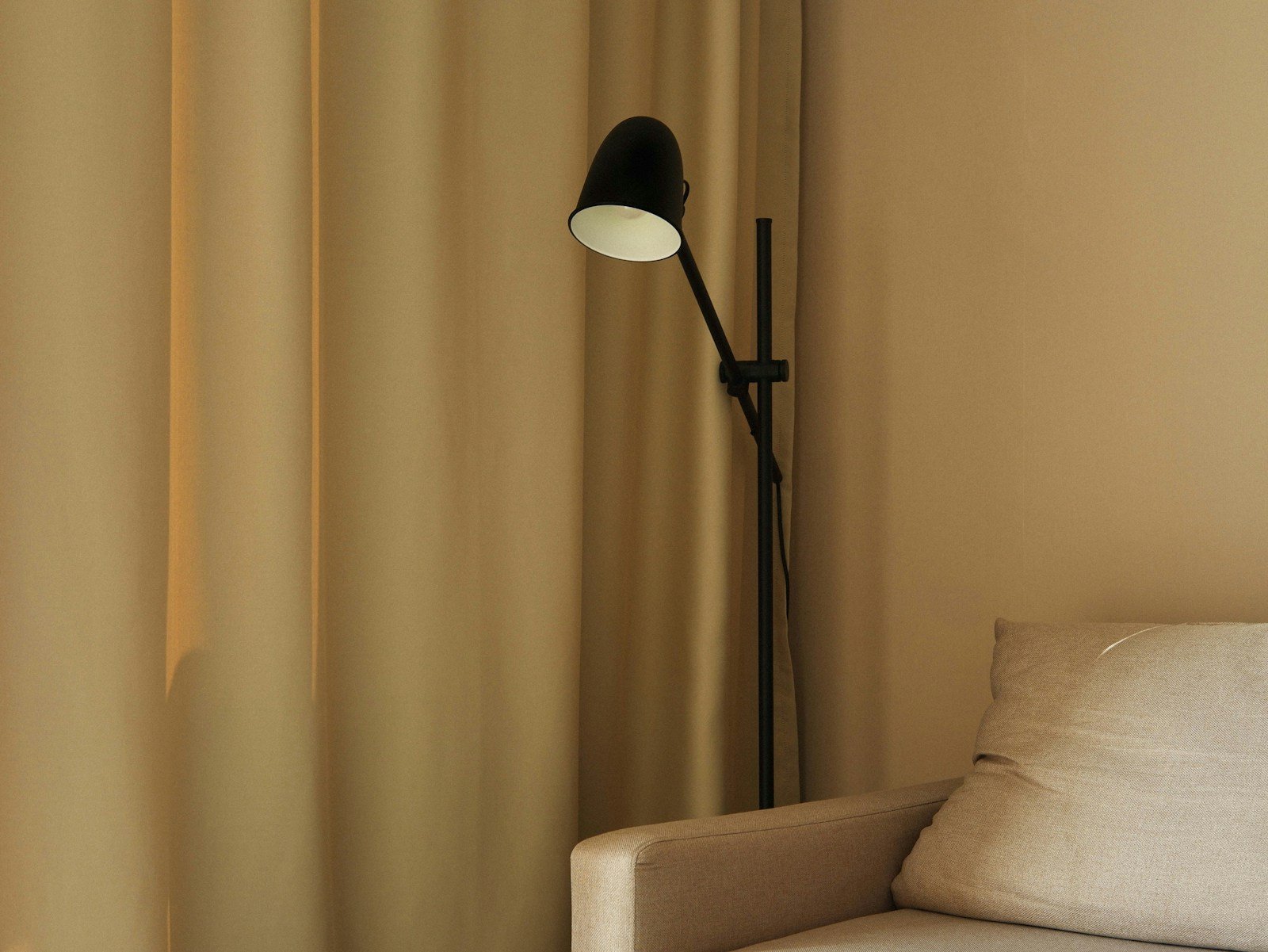 Warm lamp light and floor length curtains softening a neutral living room in the evening