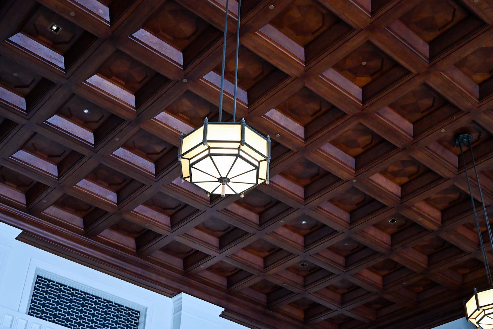 Dark wood coffered ceiling with geometric recessed panels and a central pendant light