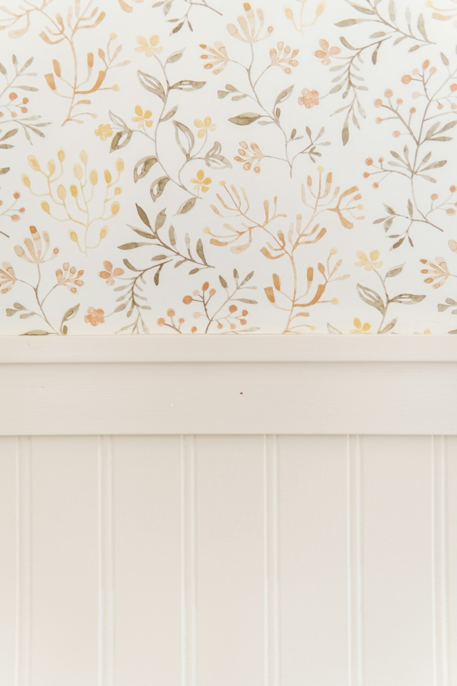 Soft botanical wallpaper in muted neutral colors above traditional wall paneling